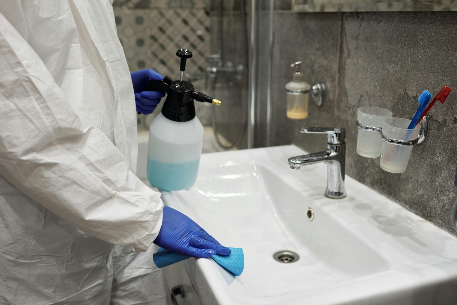 A person sanitizing a bathroom sink with a spray bottle, ensuring hygiene.