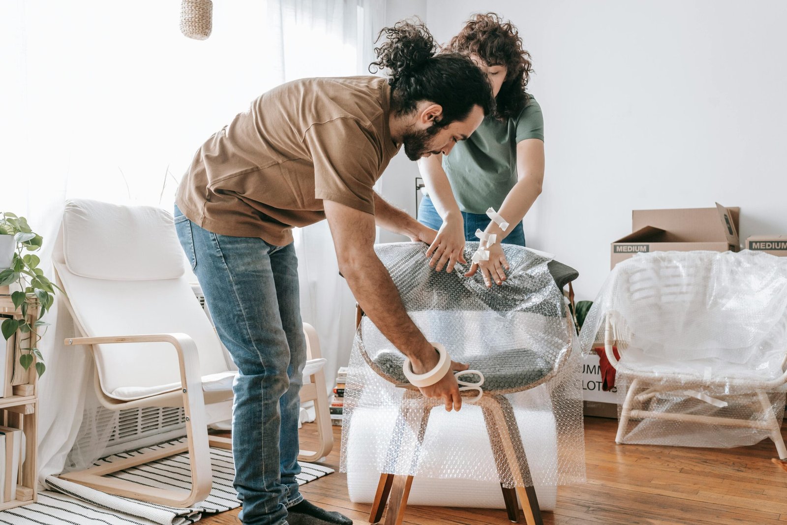 A couple carefully packs a chair with bubble wrap in their apartment, preparing for moving day.